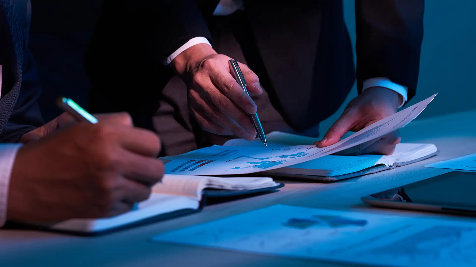 Homens de terno analisam documentos importantes, com gráficos tributários, símbolo de negócios, com foco em temáticas relacionadas a impostos.