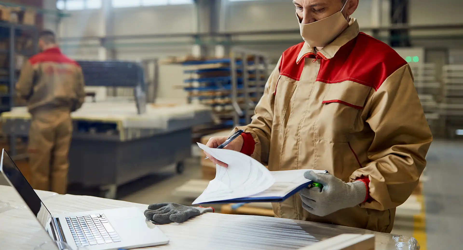 Homem funcionário de fábrica analisando documentos com máscara em ambiente industrial, representando segurança e eficiência no setor industrial.
