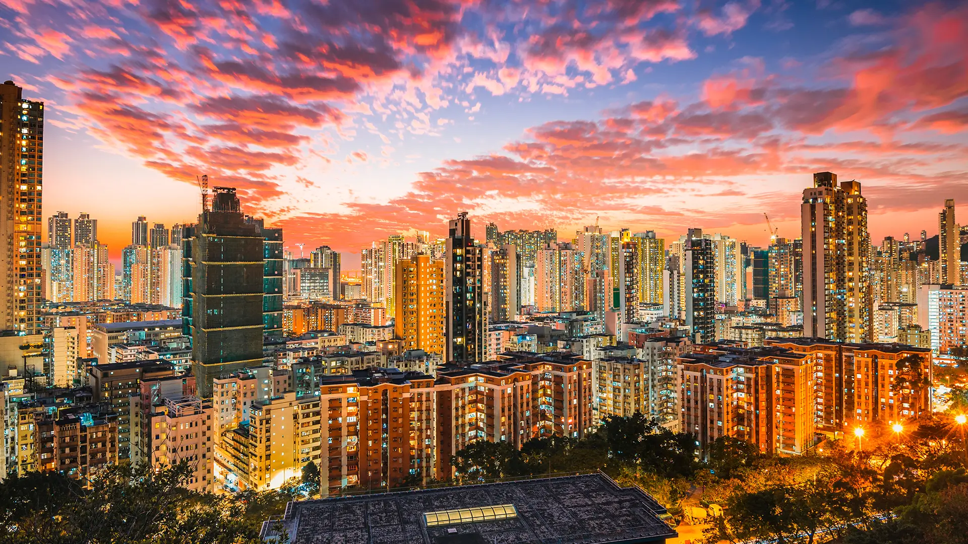 Paisagem urbana de uma grande metrópole ao entardecer, com arranha-céus modernos, céu colorido com tons de rosa, laranja e roxo, e iluminação vibrante na cidade.